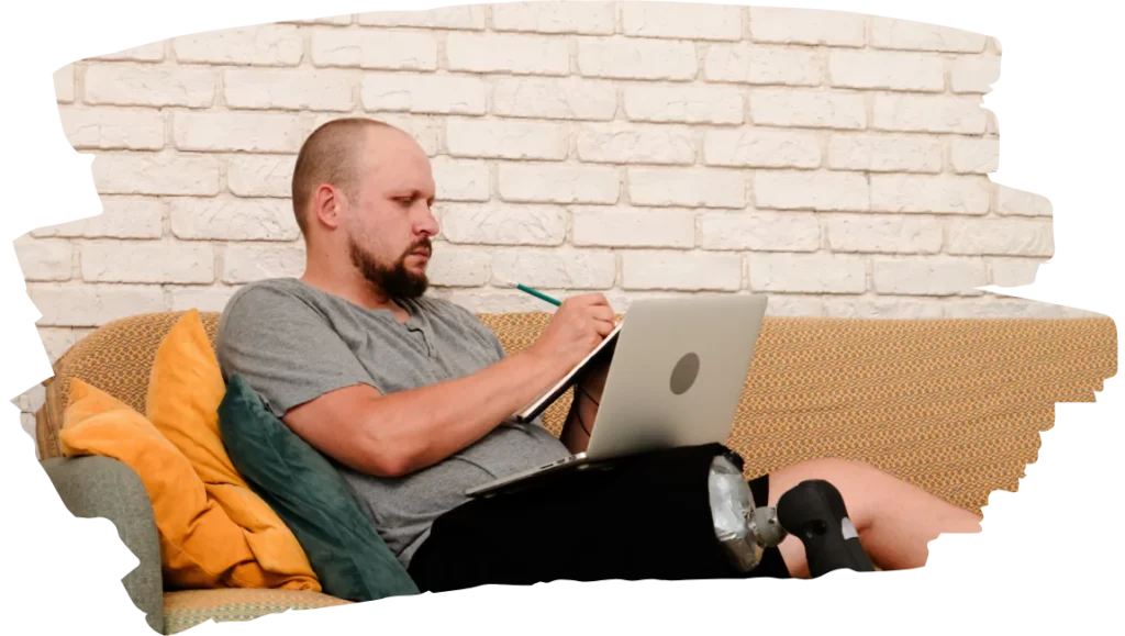 Disabled man taking notes and using laptop to contact KindNest Support Services